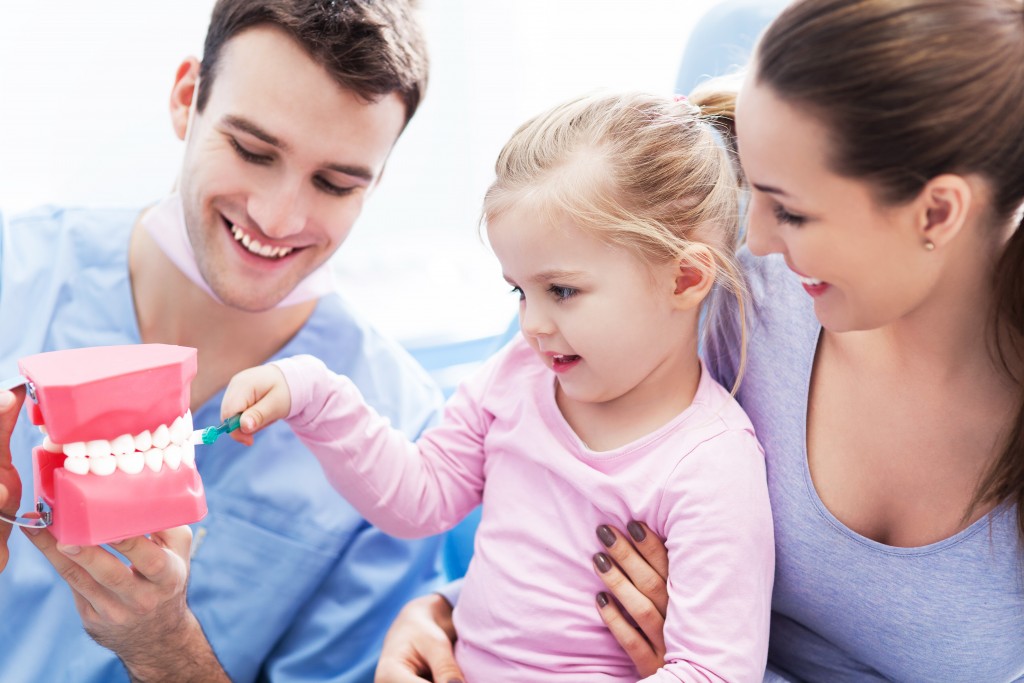 Dentist teaching young girl to brush teeth