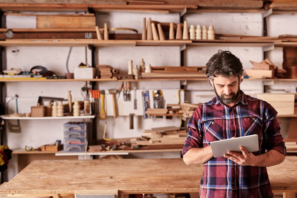 an artisan holding a tablet with woodworks at his back