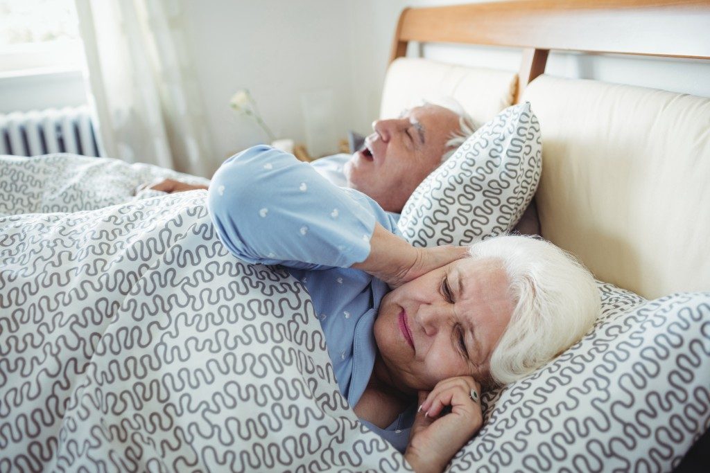 Man snoring and woman covering her ears while sleeping on bed in bedroom