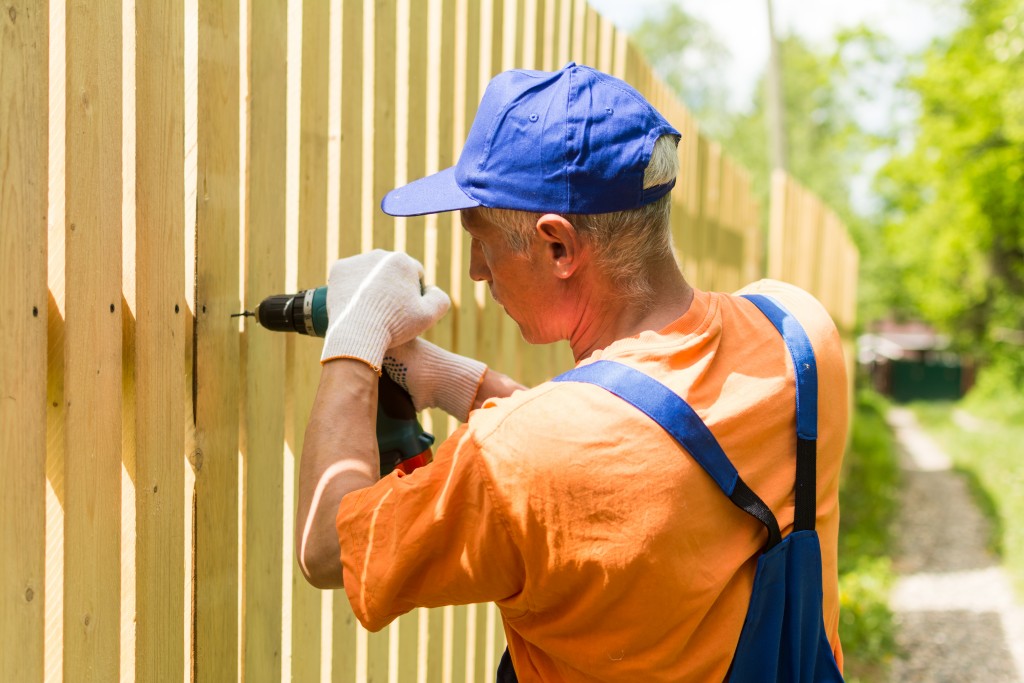 man repairing fence with a drill