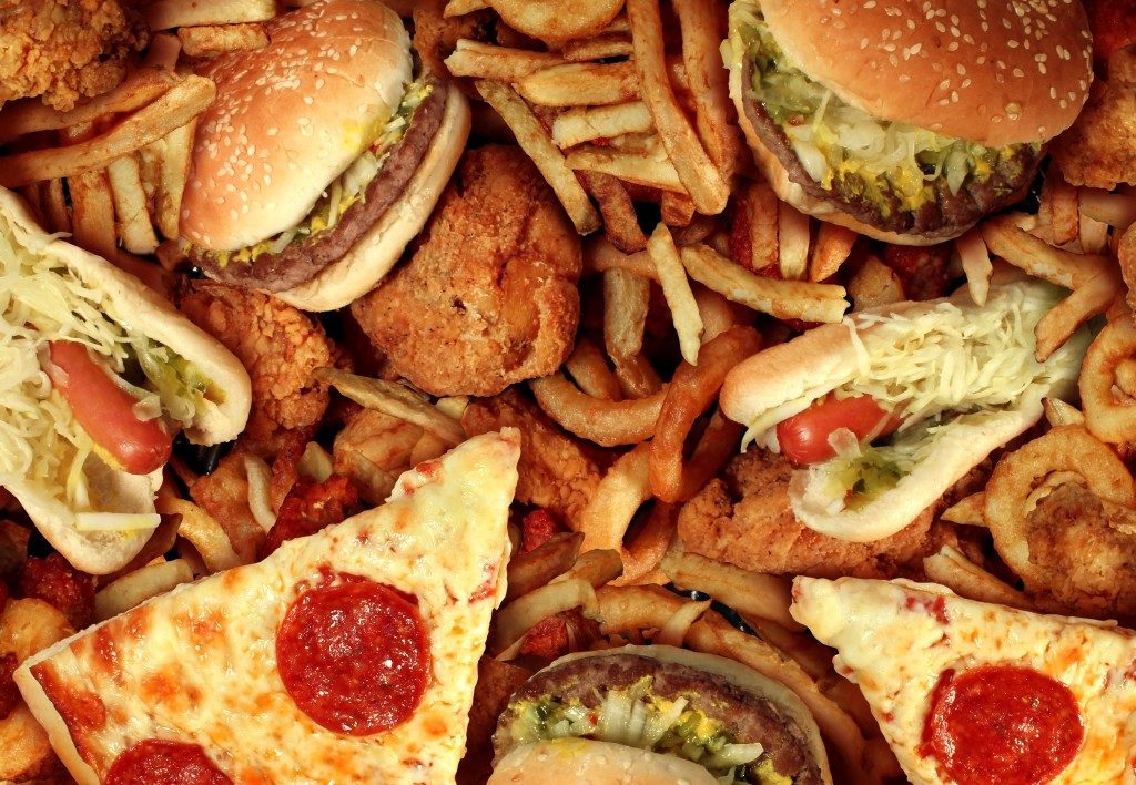 Fast food concept with greasy fried restaurant take out as onion rings burger and hot dogs with fried chicken french fries and pizza as a symbol of diet temptation resulting in unhealthy nutrition