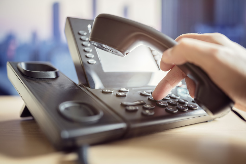 A person picking up the handset of a phone system and punching in some numbers in the office