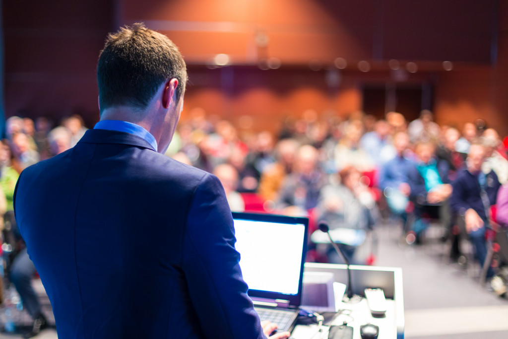 A speaker presenting at a business conference in front of many professionals