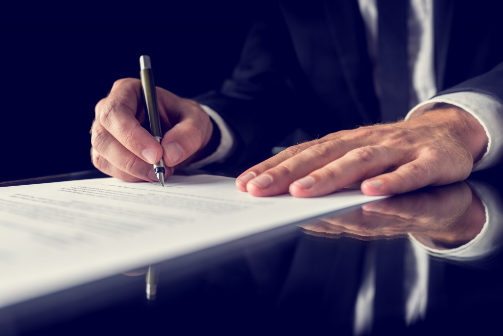 A person signing a legal document on a black desk and background