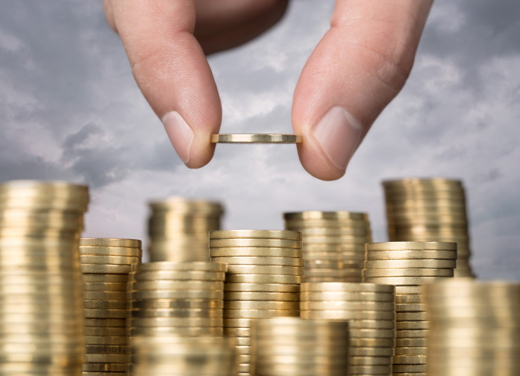 A hand stacking gold coins with a sky in the background