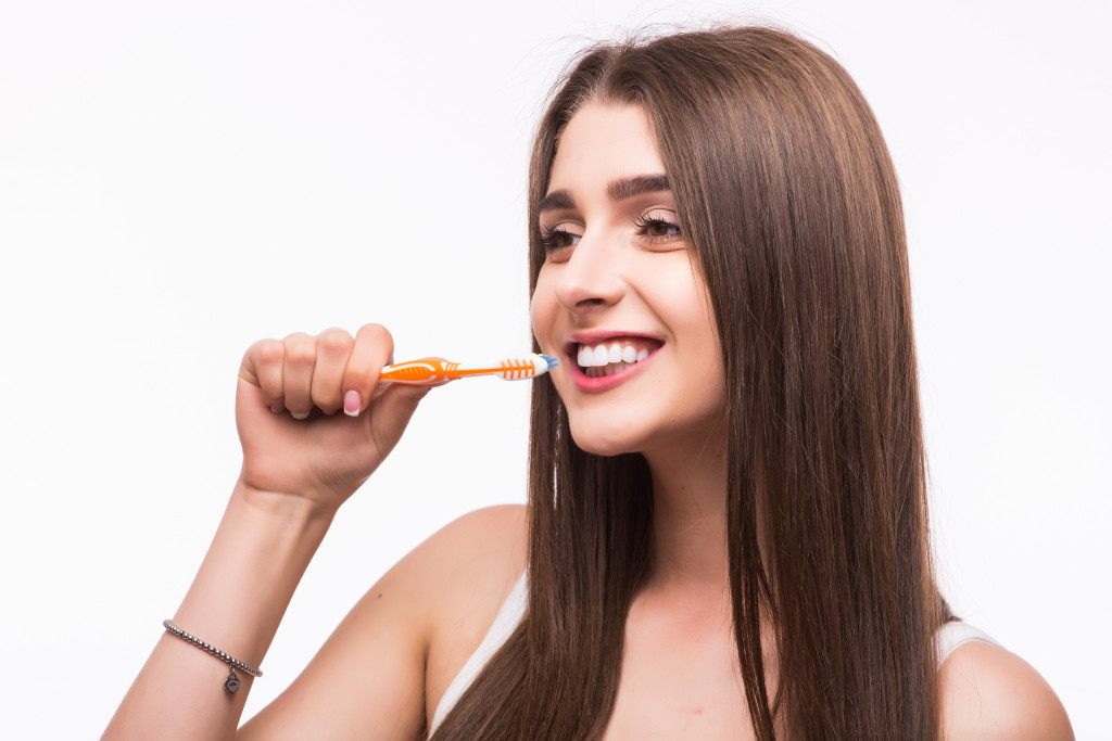 A young woman brushing her teeth with orange color brush