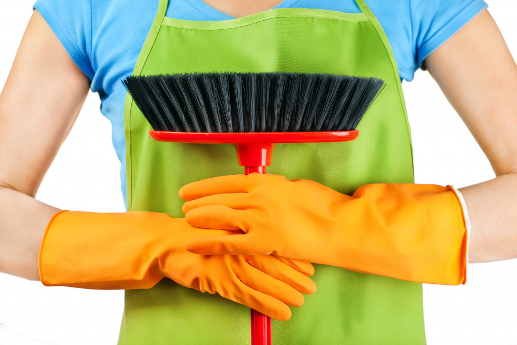 someone holding a broom wearing gloves and an apron
